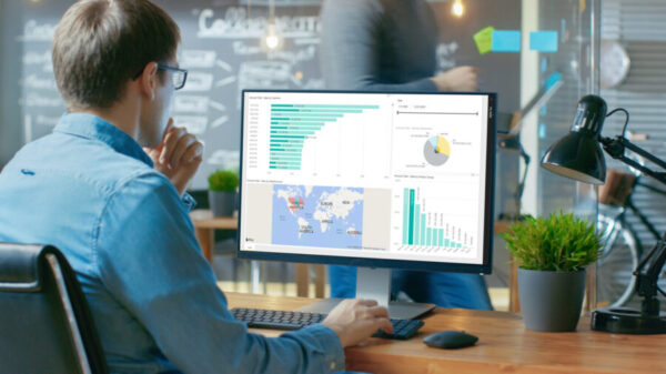 Analyst Works on a Personal Computer Showing Statistics, Graphs and Charts. In the Background His Coworker and Creative Office.