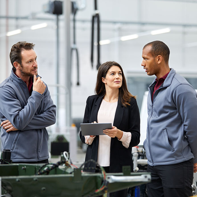 Automobile engineer discussing with colleagues in car factory. Multi-ethnic male and female professionals are standing at car production line. They are in automotive industry.