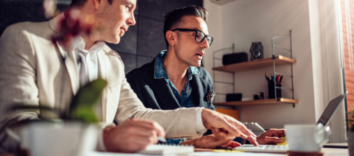 Two designers sitting at meeting table and using laptop