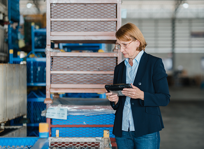 Mature caucasian female manager checks stock and inventory with digital tablet in factory warehouse. Logistic industry business.