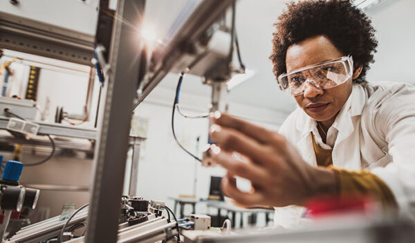 Low angle view of African American lab worker examining machine part while working in a lab.