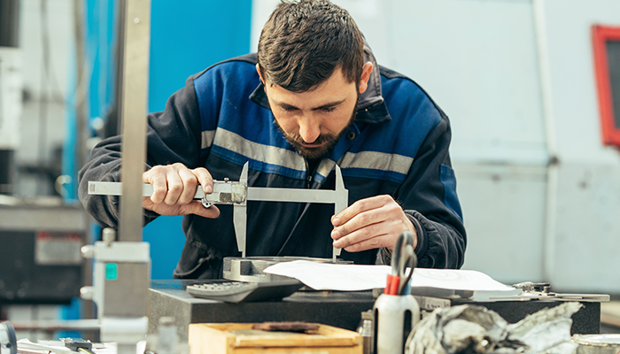 Worker measuring metal part in factory